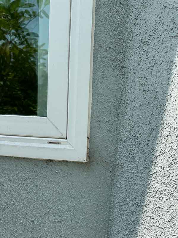 Hairline crack in exterior stucco wall above a window frame, indicating water intrusion requiring leak detection in Los Angeles